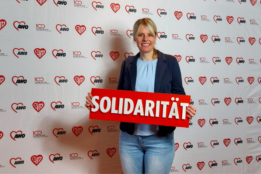 Julia Rtezlaff vor Stellwand der Arbeiterwohlfahrt mit Schild "Julia Retzlaff" in beiden Händen.