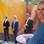 Julia Retzlaff steht an einem der Festtische und lächelt in die Kamera. Auf der anderen Seite des Tisches stehen drei Männer in festlichen Anzügen.