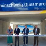 In neuen einem Tunnel stehen vier Personen unter dem Schild Gliesmarode. Vor ihnen ein Bändchen mit dem Logo der Deutschen Bahn. Sie schneiden das Band durch und eröffnen mit dieser Geste den Bahnhof offiziell.
