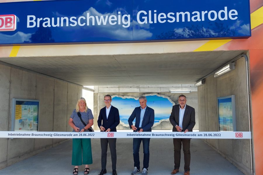 In neuen einem Tunnel stehen vier Personen unter dem Schild Gliesmarode. Vor ihnen ein Bändchen mit dem Logo der Deutschen Bahn. Sie schneiden das Band durch und eröffnen mit dieser Geste den Bahnhof offiziell.