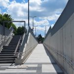 Blick aus dem Aufgang zum Bahnsteig. Neuer hellgrauer Beton bildet eine Treppe und daneben eine lange barrierefreie Rampe mit geringer Steigung.