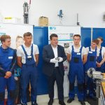 Hubertus Heil steht zwischen jungen Männern in blauen Arbeitshosen und hält eine polierte Metallkugel