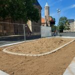 Innerhalb des Bauzaunes: Auf dem Rathausplatz (Platz der deutschen Einheit) ist auf einer Plastikplane Erde aufgeschüttet. Ein Teil ist gleichmäßig verteilt. In der Mitte ist ein Haufen in einem Kreis aus Pflastersteinen. Im Hintergrund sieht man den Bauzaun und dahinter die Münzstraße am Dom.