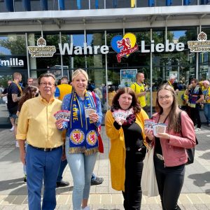 Julia Retzlaff und drei weitere Personen stehen vor der Wahren Liebe und halten die Spielplaner in die Kamera.