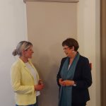 Julia Retzlaff und Birgit Hone stehen vor einer schlichten Wand im Rathaus und unterhalten sich miteinander