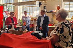 In einer Werkstatt stehen um eine Werkbank mehrere Personen im Gespräch. Sozialministerin Daniela Behrens ist einer Seniorin zugewandt. Julia Retzlaff, Christoph Bratmann und Annette Schütze beteiligen sich an dem Austausch.