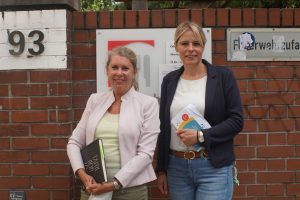 Annette Schütze und Julia Retzlaff stehen vor dem Eingang der Tafel. Beide haben Notizbücher in der Hand.