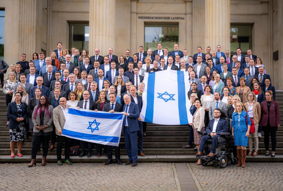 Die Fraktionen von SPD, CDU und Bündnis90/Grüne stehen auf den Stufen des Portikus vor dem Landtag mit zwei großen israelischen Fahnen.